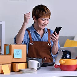 Successful mature Asian woman entrepreneur, Business owner with arm up happy while looking at her online order from smartphone